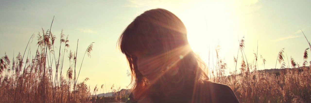 woman standing in a filed of tall grass with the sun behind her