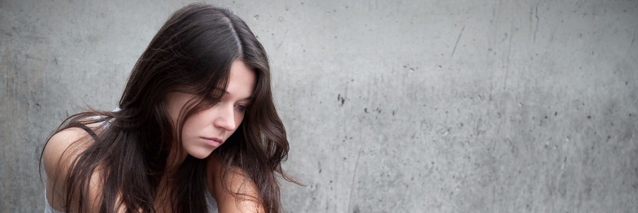 Lessons From My Battle With Mental Illness troubled teenaged girl sitting alone in front of gray wall