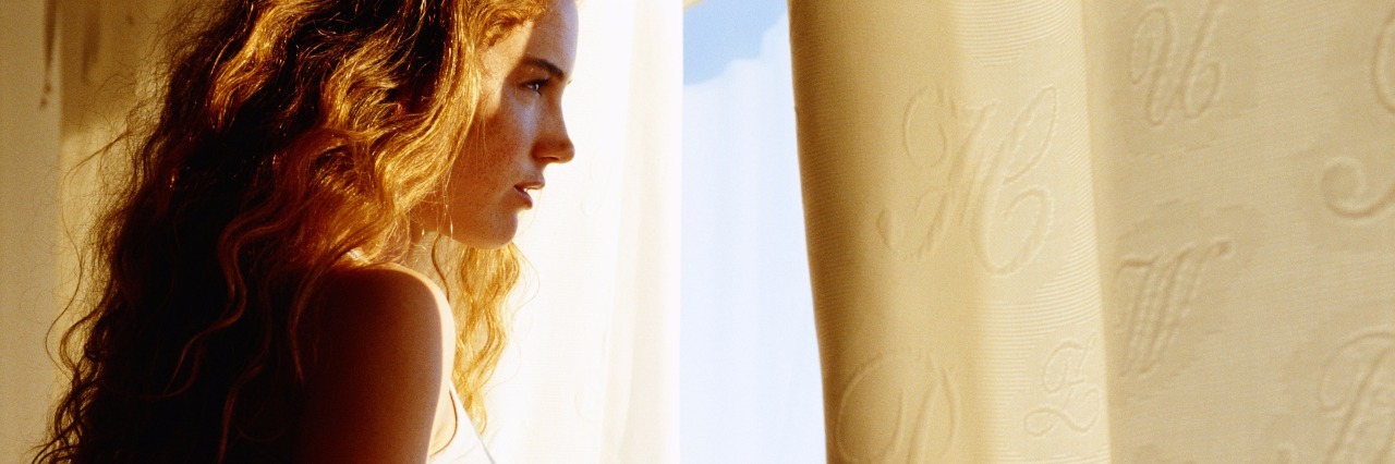 How to Fight Depression on Bad Days young woman parting curtains and looking out the window