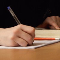 Student in classroom taking notes next to open book on table