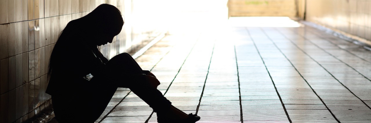 Explaining My PTSD to My Loved Ones woman sitting in a hallway in darkness