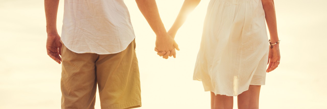 young couple dressed in white holding hands and standing on the beach during sunset