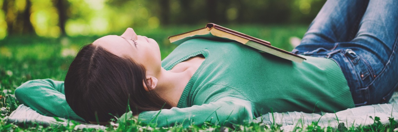 Positive Outcomes and Lessons Learned From Chronic Illness woman relaxing on her back in a grassy field with an open book on her chest