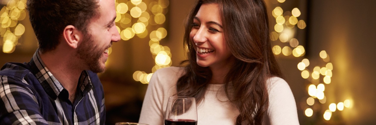 couple on a date in a bar. man is drinking beer and woman is drinking wine. lights are twinkling in the background.