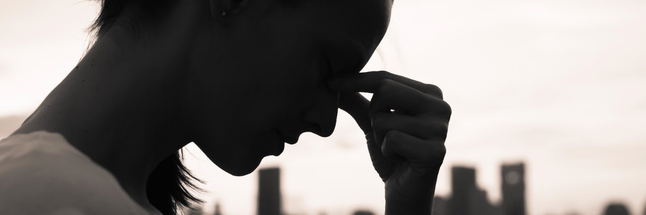 Information About Concussions This Mom Wishes She'd Known Black and white photo of woman in front of city landscape with eyes closed and fingers on the bridge of her nose