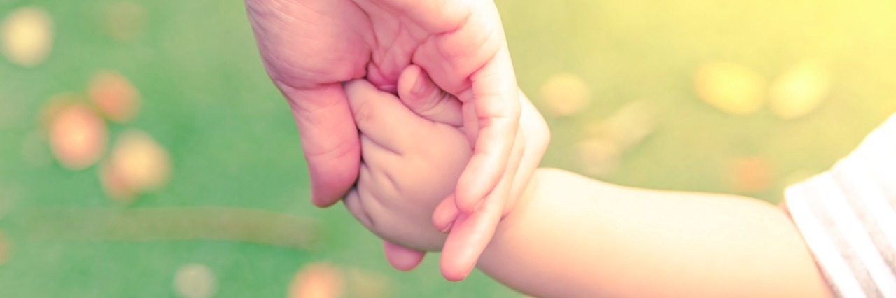 A Mother's Response to the UK’s New Prenatal Test for Down Syndrome Parent holding baby's hand outdoors