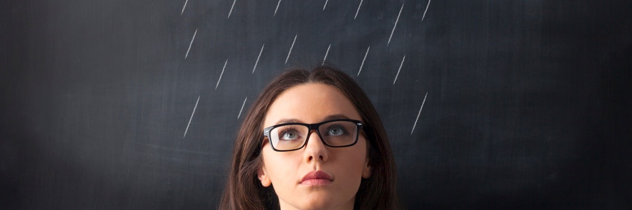 woman standing in front of chalkboard with rain clouds drawn above her head