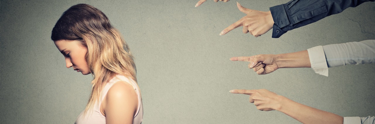 woman hanging her head with several people pointing fingers at her