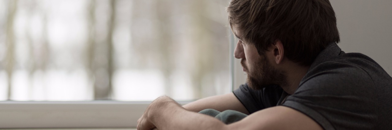 How to Love a Guy With Anxiety sad man looking out window while hugging his knees