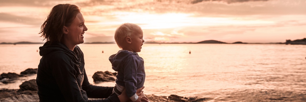 Parenting: Feeling Guilty as a Mother With a Chronic Illness mother and son sitting on rocky ledge looking at a sunset over the ocean