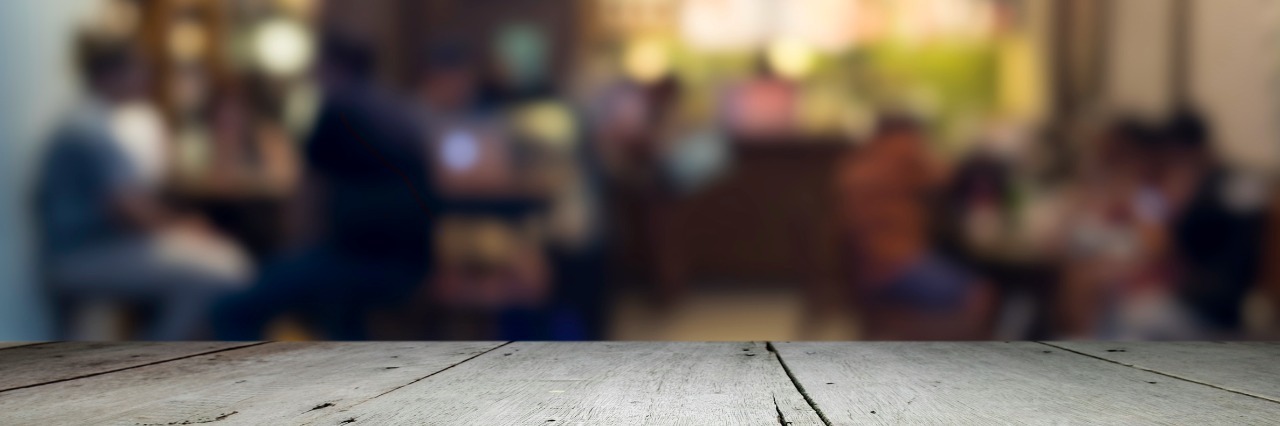 Thanksgiving Without a Tribe empty wooden table with party going on in the background