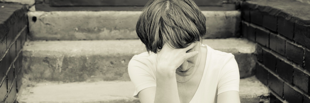 The Collision of Mental Health and Substance Abuse A woman sits on the concrete stairs in a very depressed mood, lying next to her on the stairs is her backpack.