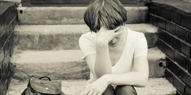 The Collision of Mental Health and Substance Abuse A woman sits on the concrete stairs in a very depressed mood, lying next to her on the stairs is her backpack.