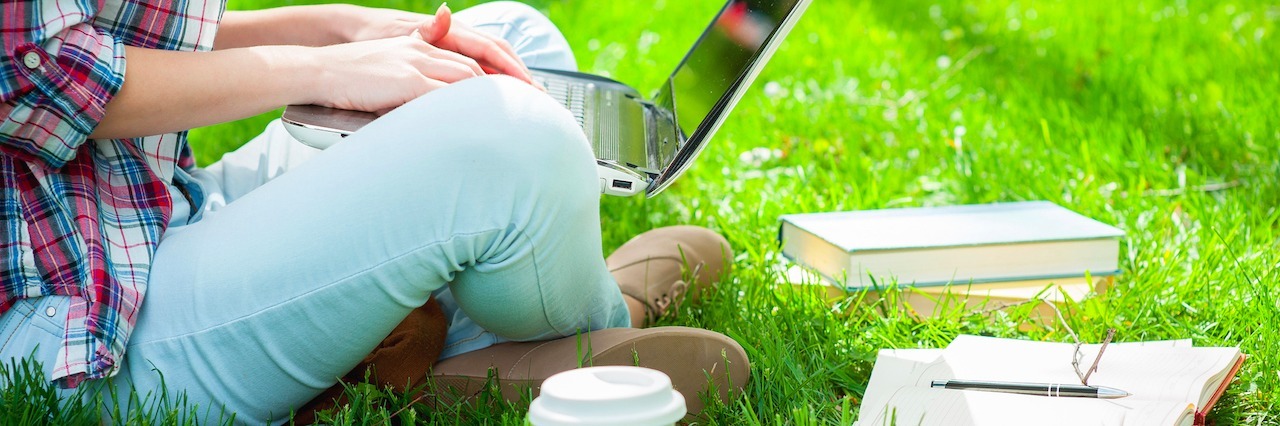 female student working on laptop while sitting in a park