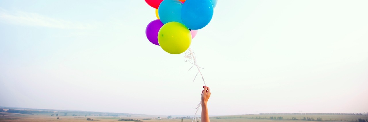 How to Define Your Worth When You're Unemployed With a Mental Illness hand holding colorful balloons