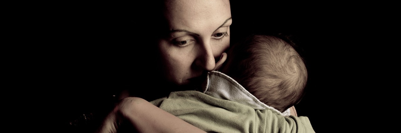 mother holding her child tightly to her chest against black background
