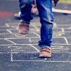 Child playing hopscotch on playground outdoors.