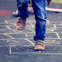 Child playing hopscotch on playground outdoors.