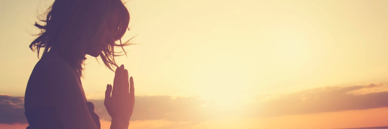 Using Serenity Prayer and Mantras to Cope With Chronic, Mental Illness woman meditating and praying on a beach during sunset