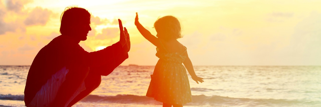 parent high fiving young daughter at the beach