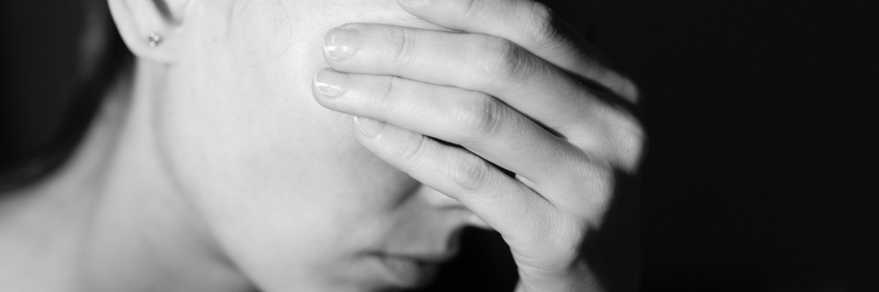 a woman covering her eyes with her hand looking stressed against black background