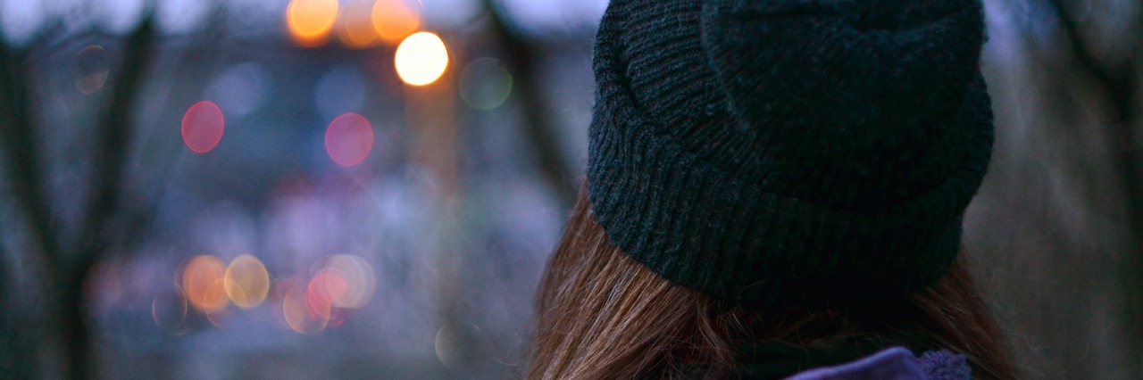Dealing With Misconceptions About Being on the Autism Spectrum Woman wearing beanie, looking at city lights through tree branches