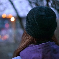 Woman wearing beanie, looking at city lights through tree branches