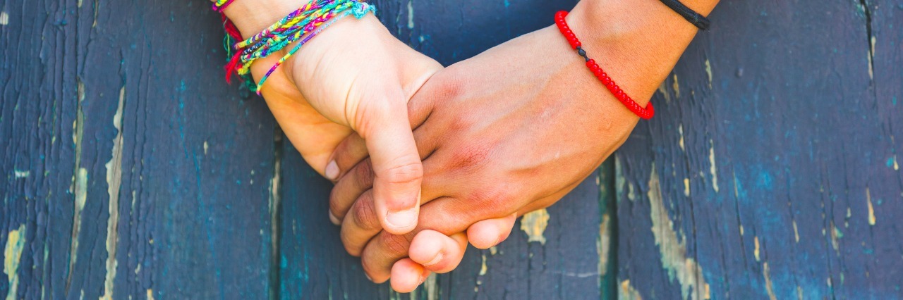 close up on two women holding hands in front of wooden background