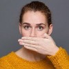 woman in a yellow sweater covering her mouth with her hand