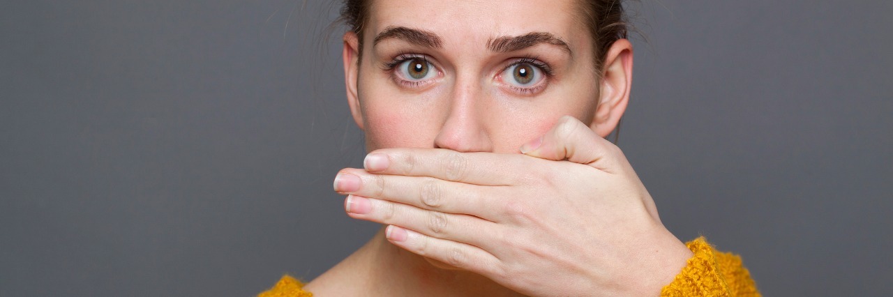 Tourette Syndrome: It's Not Just About Cursing woman in a yellow sweater covering her mouth with her hand