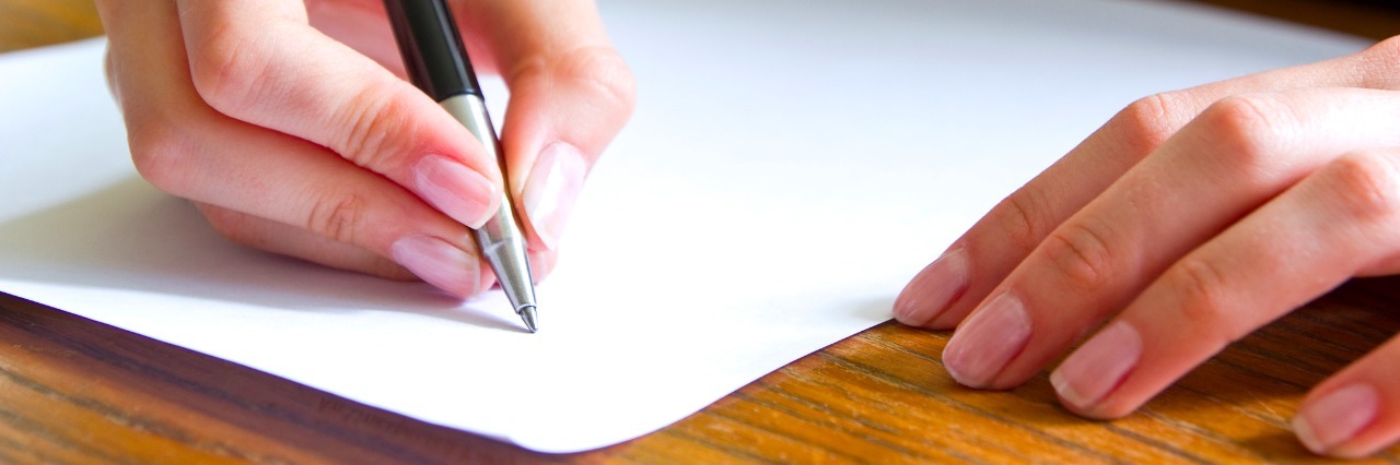 close up of a womans hands writing on a sheet of paper at a desk