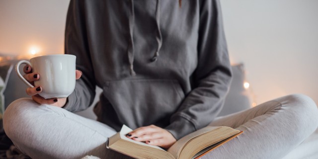 Girl drinking hot tea and reading book in bed