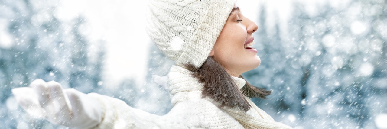 Feeling Thankful With Ehlers-Danlos Syndrome woman in white hat, jacket, and mittens stands outside enjoying the snow