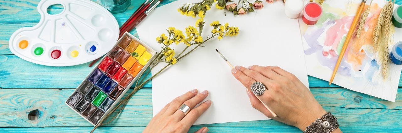 Ways to Distract Yourself From Chronic Pain person painting with watercolors on blue wooden table