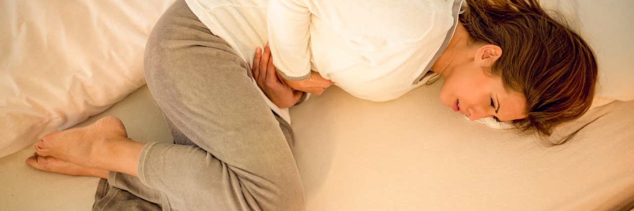 When Gastroparesis Feels Like a Prison Cell young woman lying on bed and holding hands on her stomach.