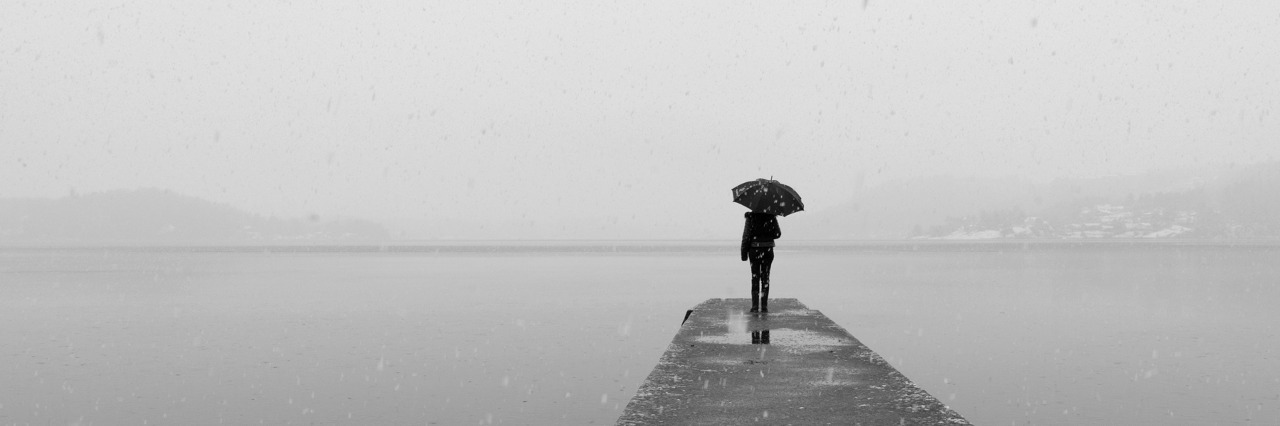 lonely woman with an umbrella standing alone on a dock under a grey sky