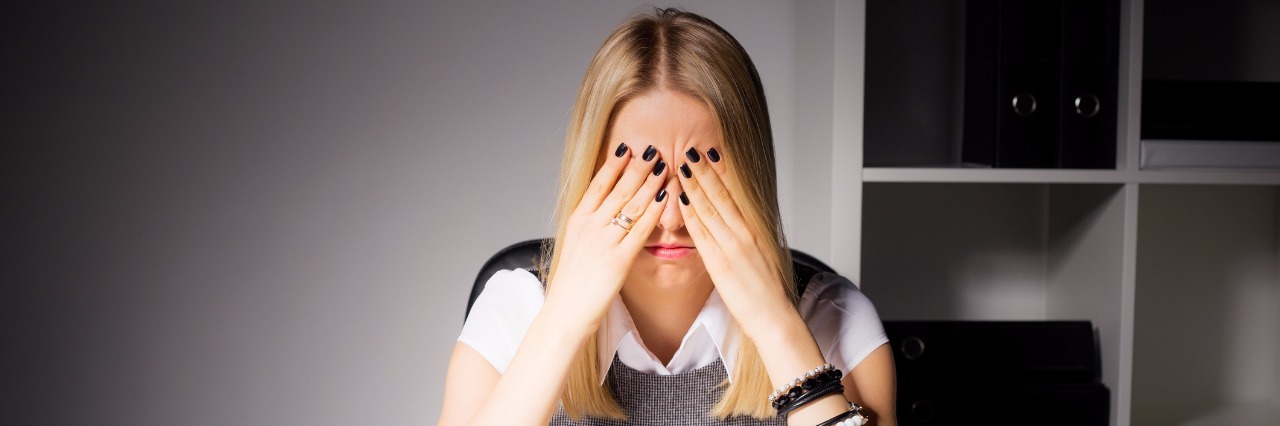 Taking Mental Health Days woman sitting in her office with her eyes covered by her hands