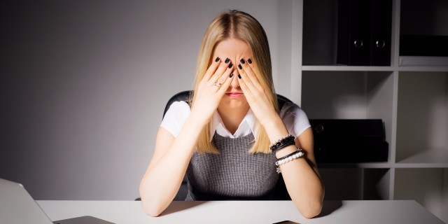 woman sitting in her office with her eyes covered by her hands