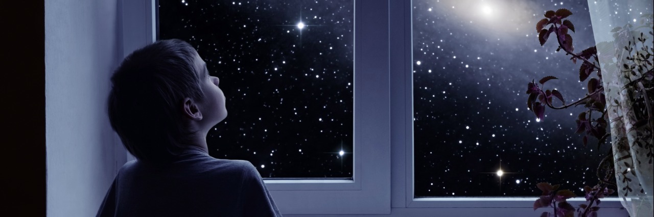 little boy looking out a window at the night sky