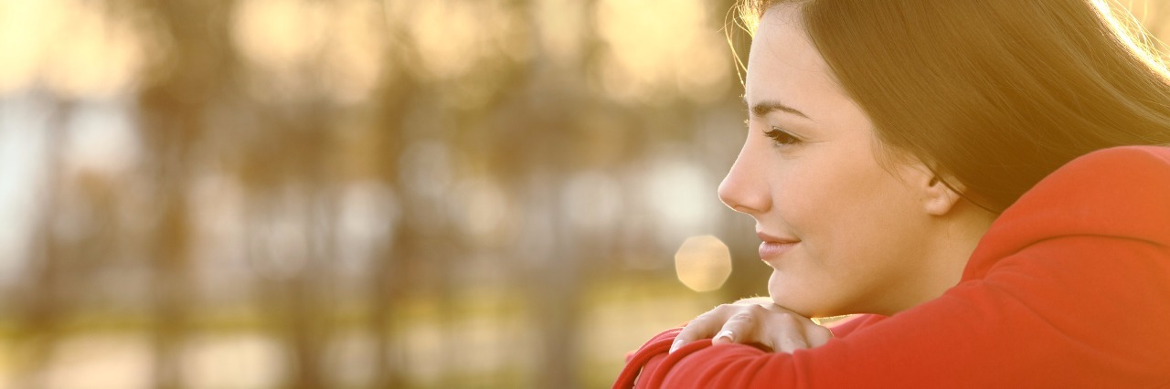 Thoughts on Inflammatory Bowel Disease One Month After Diagnosis woman in red shirt leaning on wooden railing and looking at sunset