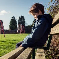 sad boy sitting on a bench by a playground