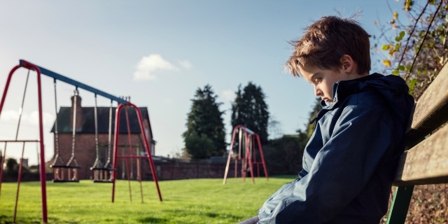 sad boy sitting on a bench by a playground