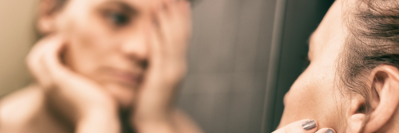 Sharing Your Suicidal Thoughts With a Therapist A sad woman looking in the mirror, covering her face with one of her hands