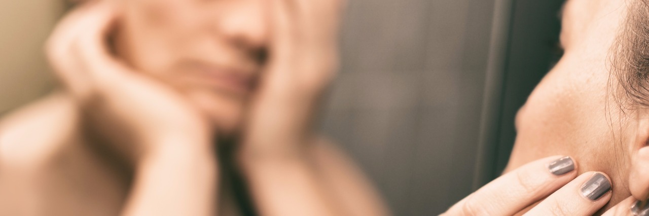 Feeling Like I Lead a Double Life With Fibromyalgia Mirror reflection of woman with one hand over her eye and the other hand on the side of her face