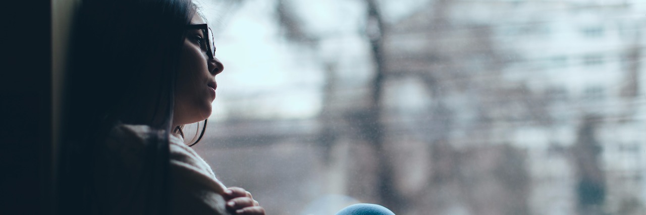 Battling Mental Illness During the Holiday Season sad young woman sitting by window and looking outside