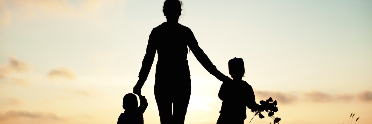 Mother holding hands with two children at sunset