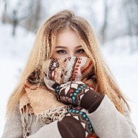 blonde woman standing outside in the snow wearing a heavy coat, scarf, and gloves