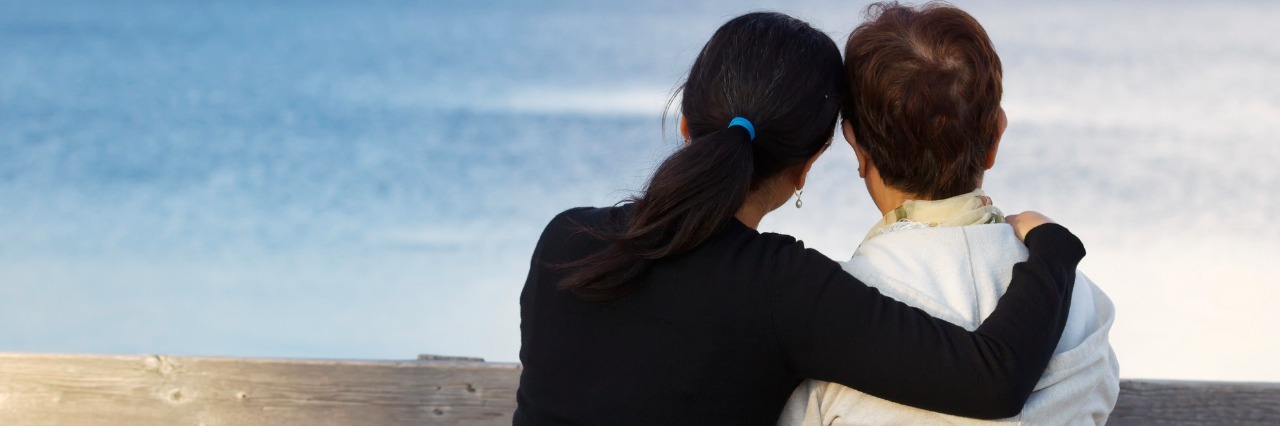 What to Do When A Loved One Is Diagnosed with Lupus Closeup of mother with mature daughter holding her while sitting on wooden bench looking outward at the lake