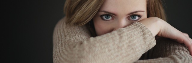 woman in light brown sweater crossing her arms and covering part of her face