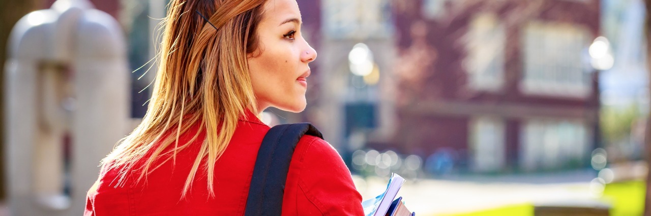 Tips for College Students With Chronic Migraines woman walking on college campus holding books and carrying backpack